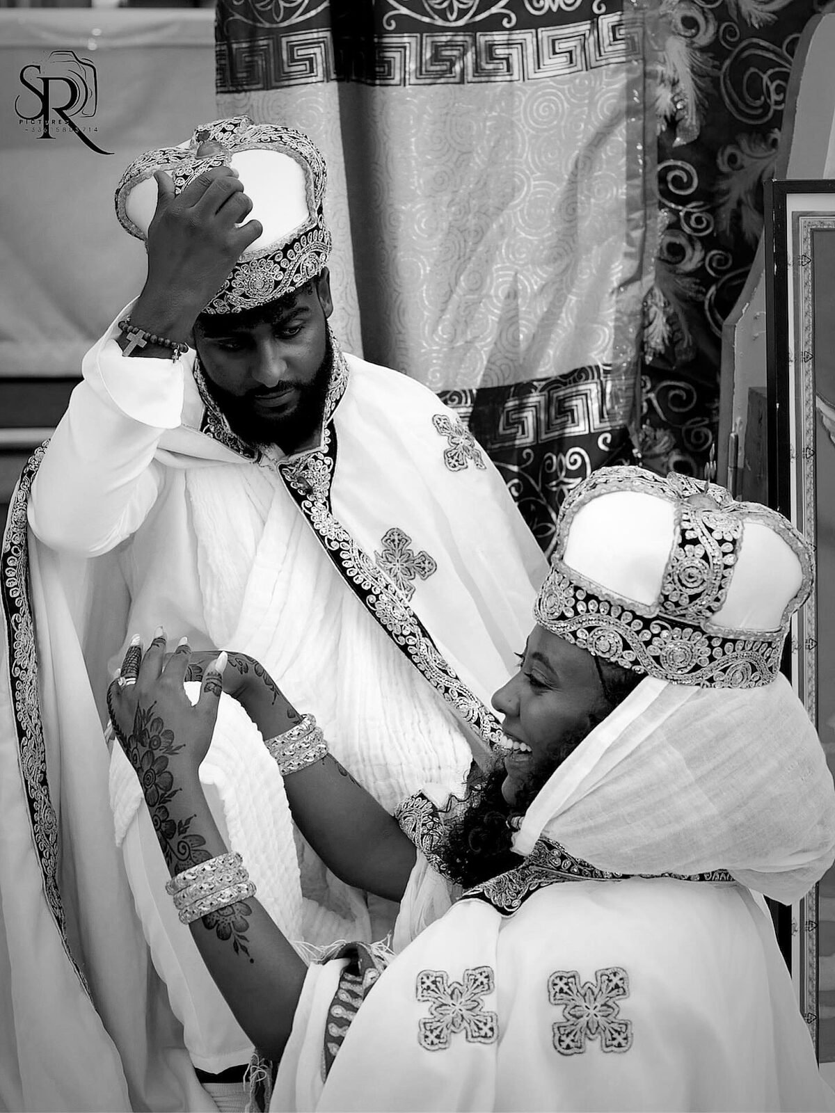Portrait serré des mariés en tenue de cérémonie, couronnes et capes brodées, en noir et blanc