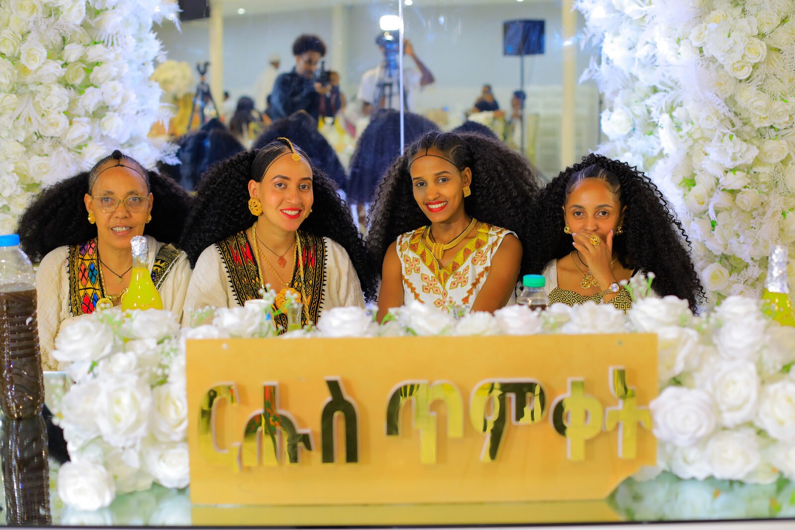Quatre femmes en tenue traditionnelle posent derrière un panneau fleuri portant une inscription en amharique