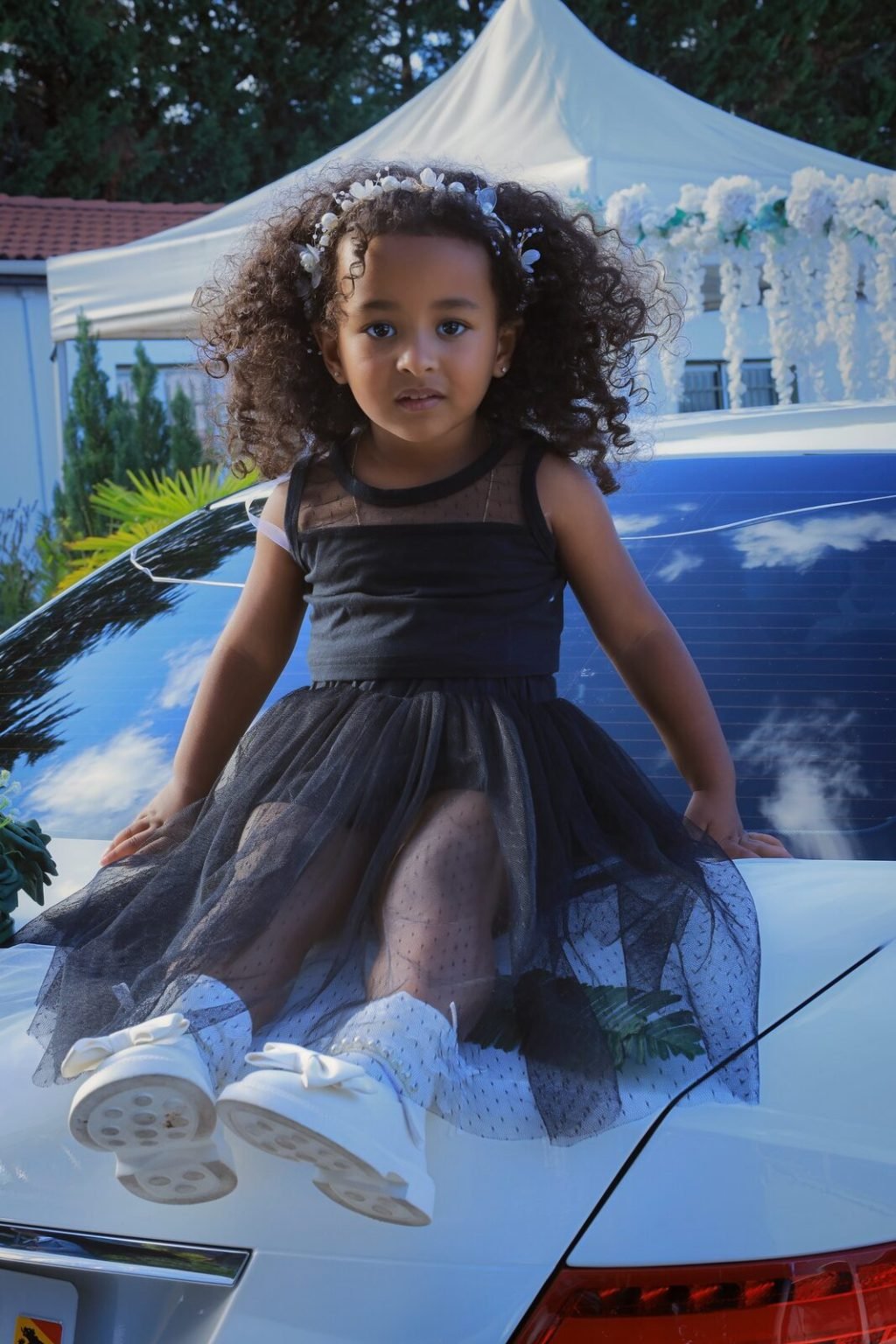 Une fillette en robe de tulle noire assise sur le capot d'une voiture