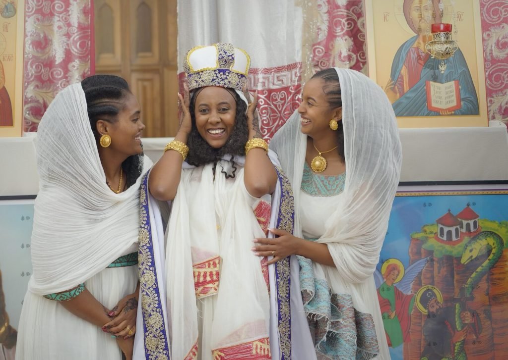 Trois femmes en tenue traditionnelle blanche brodée, souriantes, dans l'église