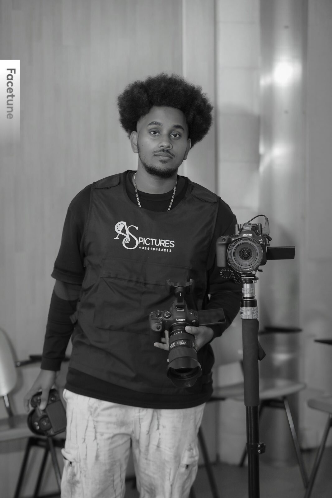 Portrait de Samey en noir et blanc, appareil photo en main devant son trépied