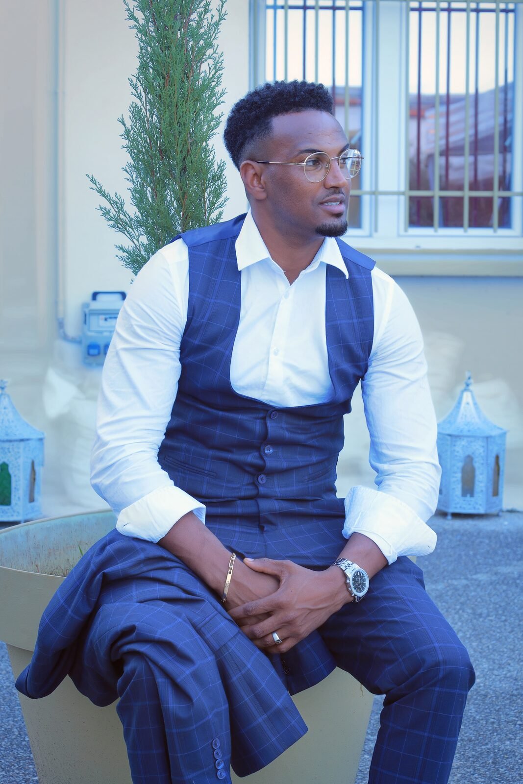 Un homme en gilet bleu et chemise blanche, assis, regard vers l'objectif
