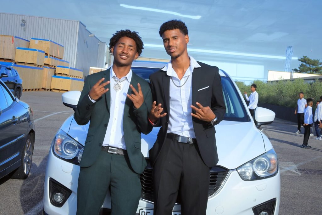 Deux hommes en costume posent devant une voiture blanche, jour de mariage