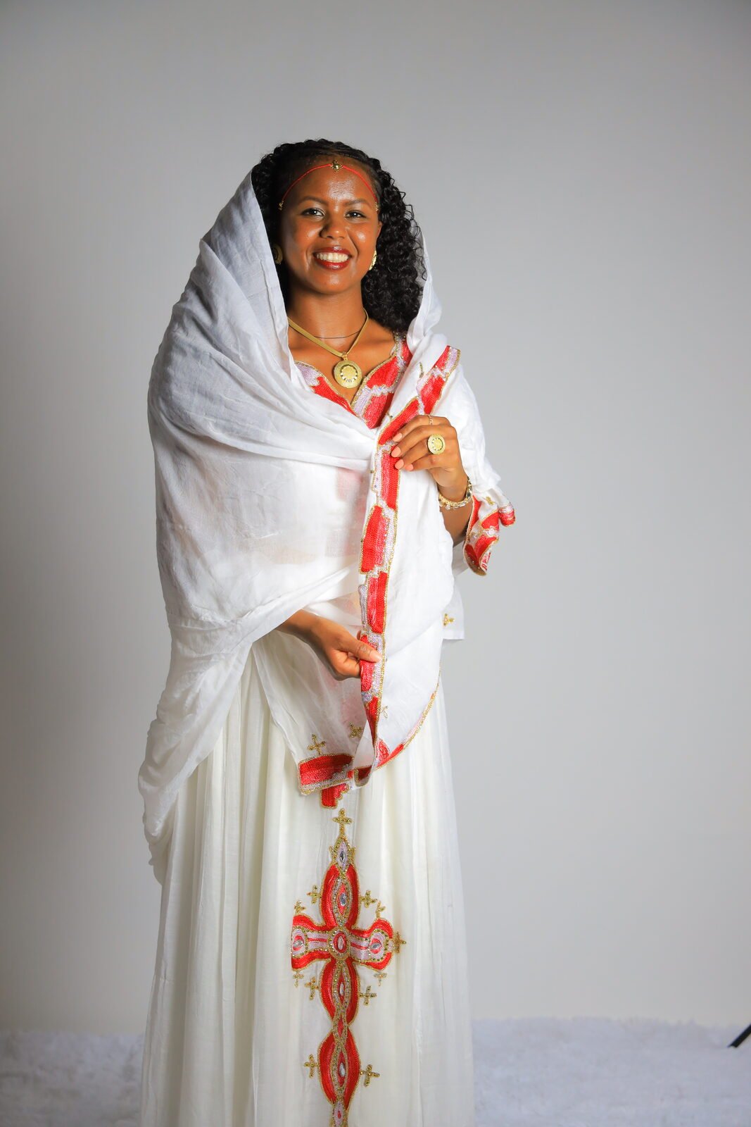 Portrait en studio, tenue blanche brodée de rouge, croix en pendentif
