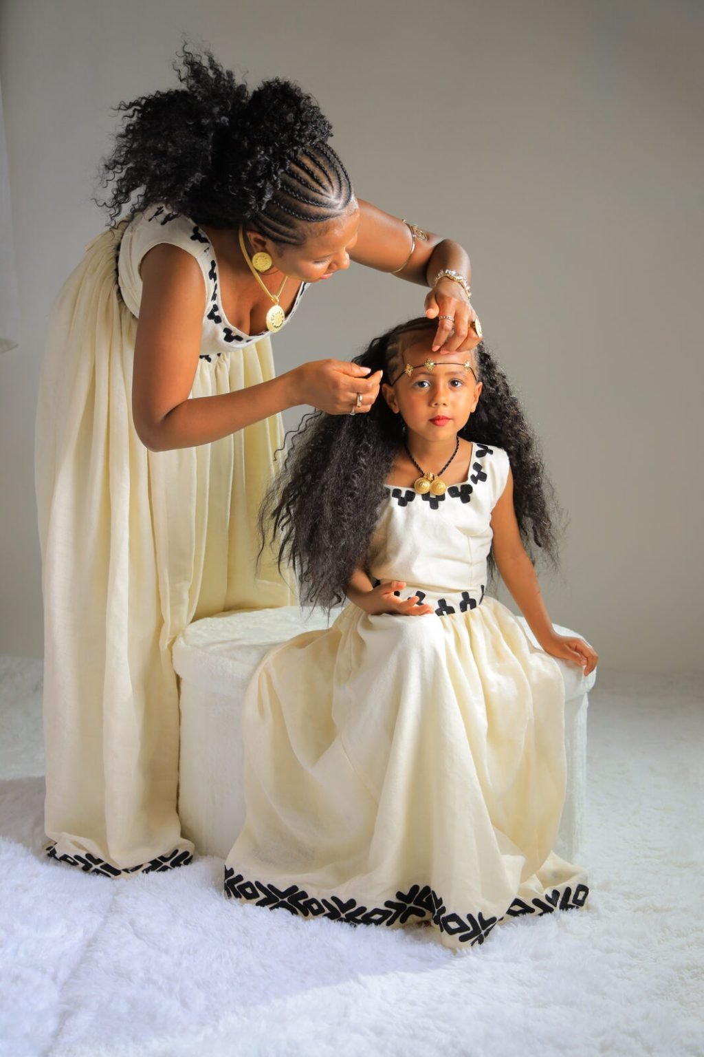 Une mère arrange les cheveux de sa fille, toutes deux en tenue traditionnelle