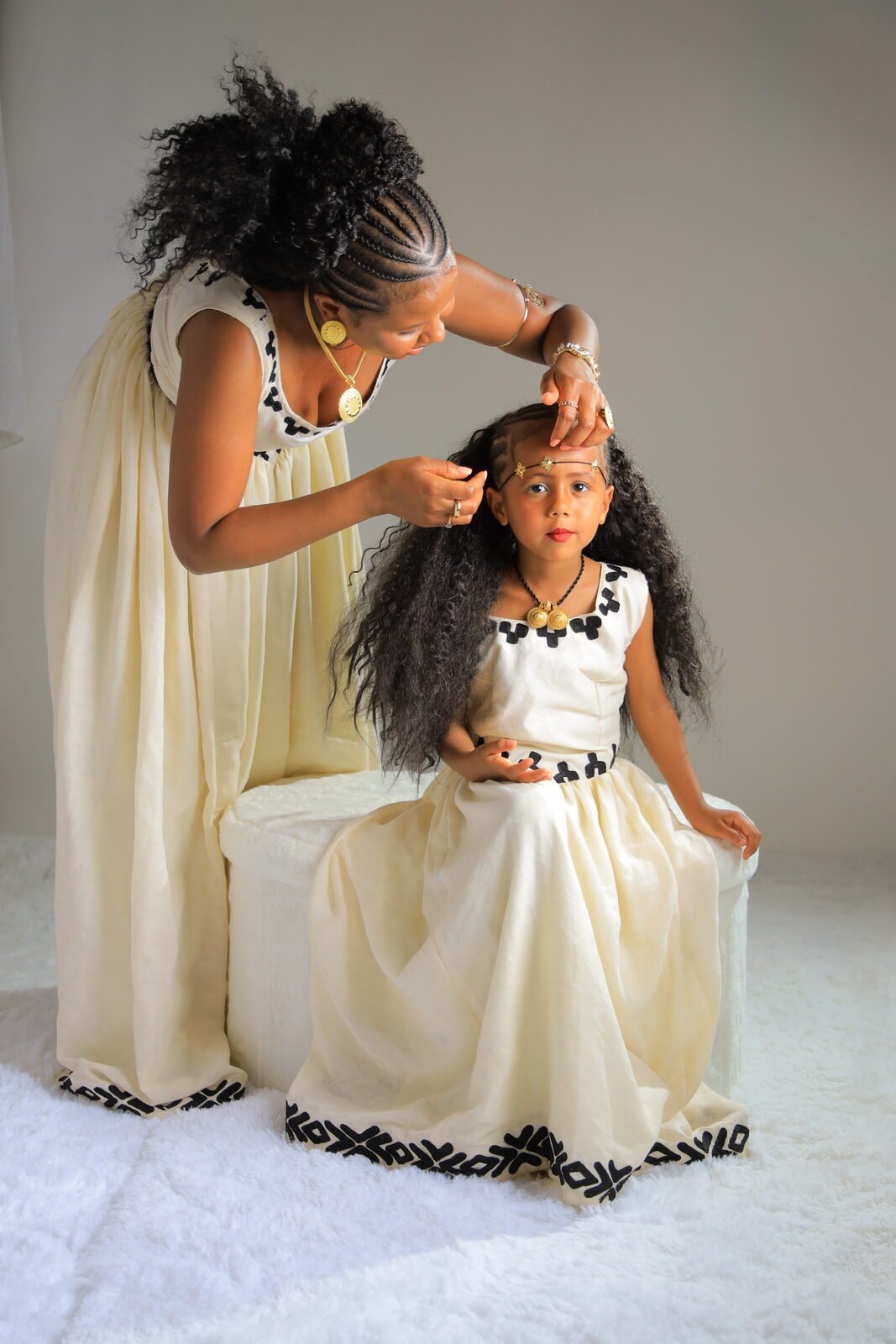 Une mère arrange les cheveux de sa fille, toutes deux en tenue traditionnelle