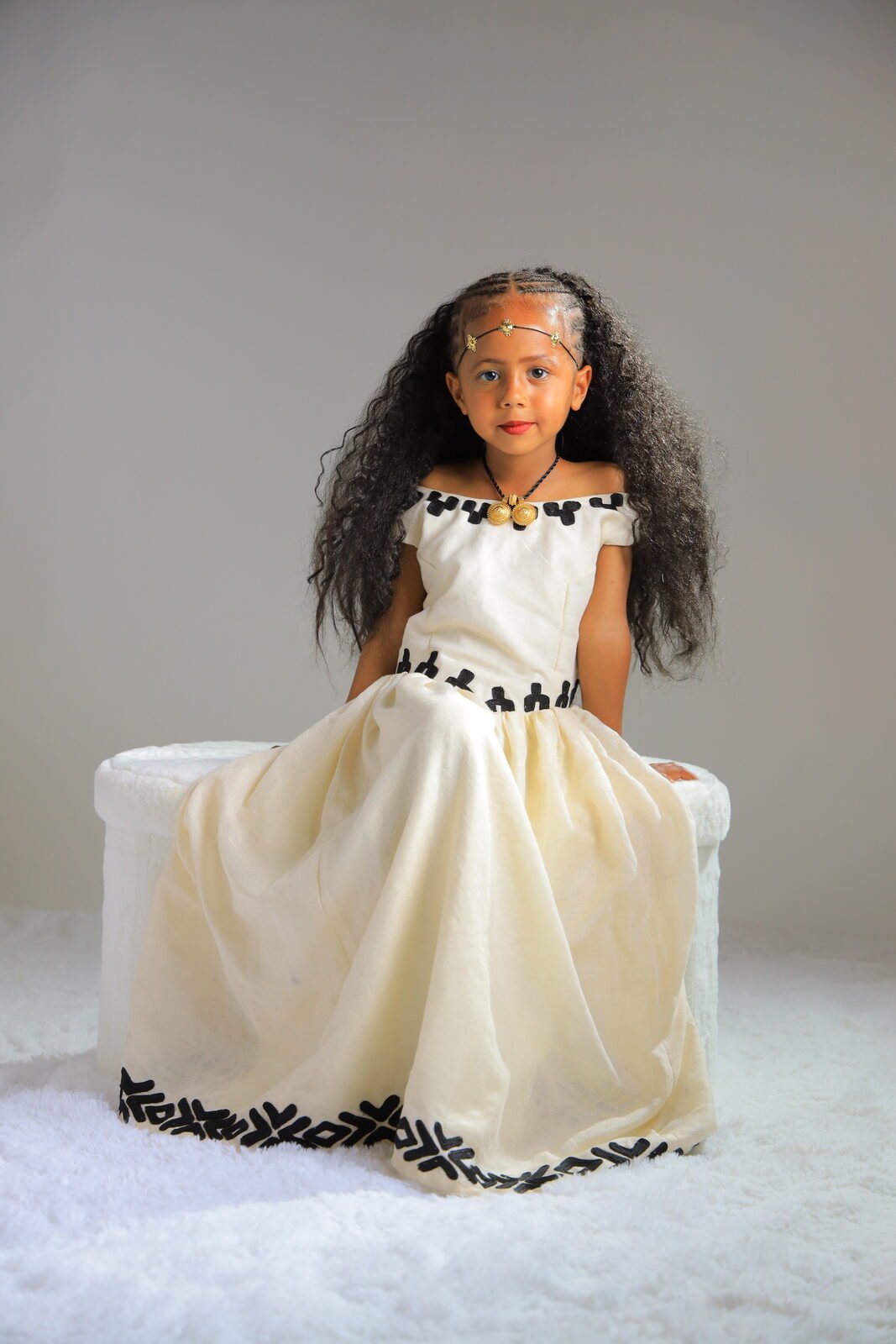 Une fillette en robe traditionnelle assise, studio sur fond clair