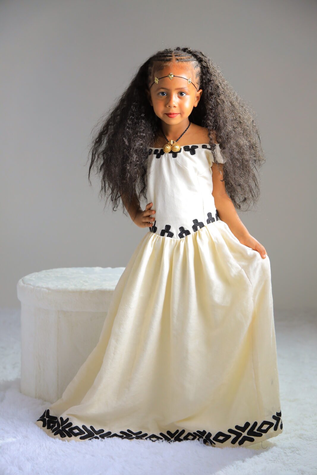 Une fillette en robe traditionnelle assise sur un cube blanc, studio