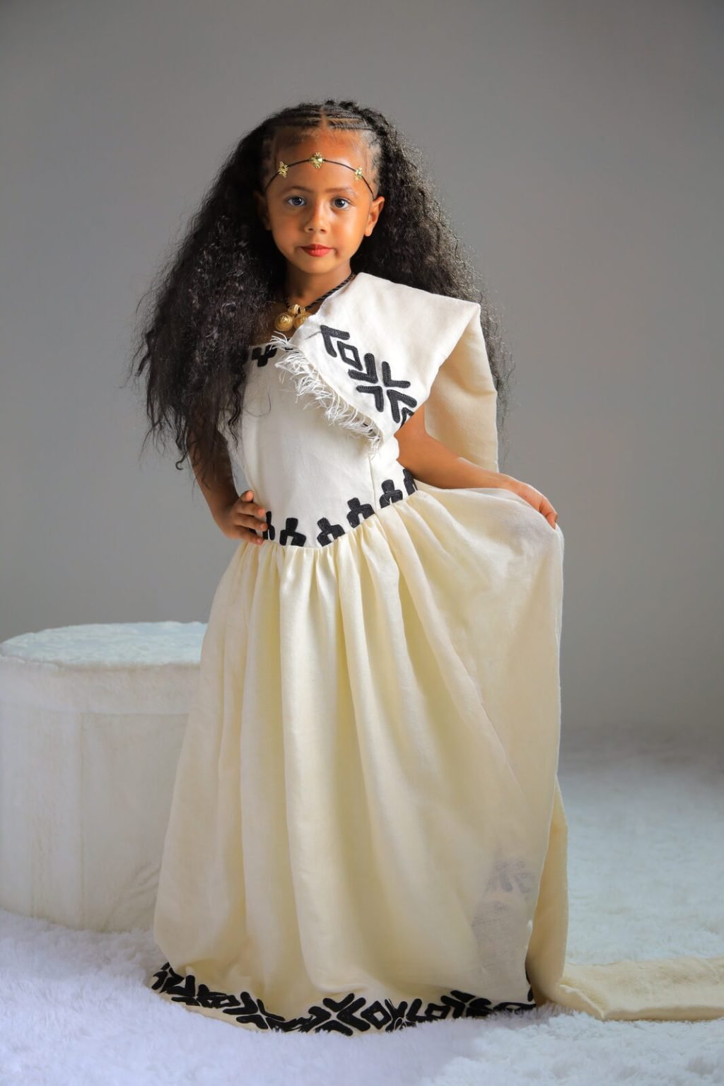 Une fillette en robe traditionnelle tenant sa jupe, studio