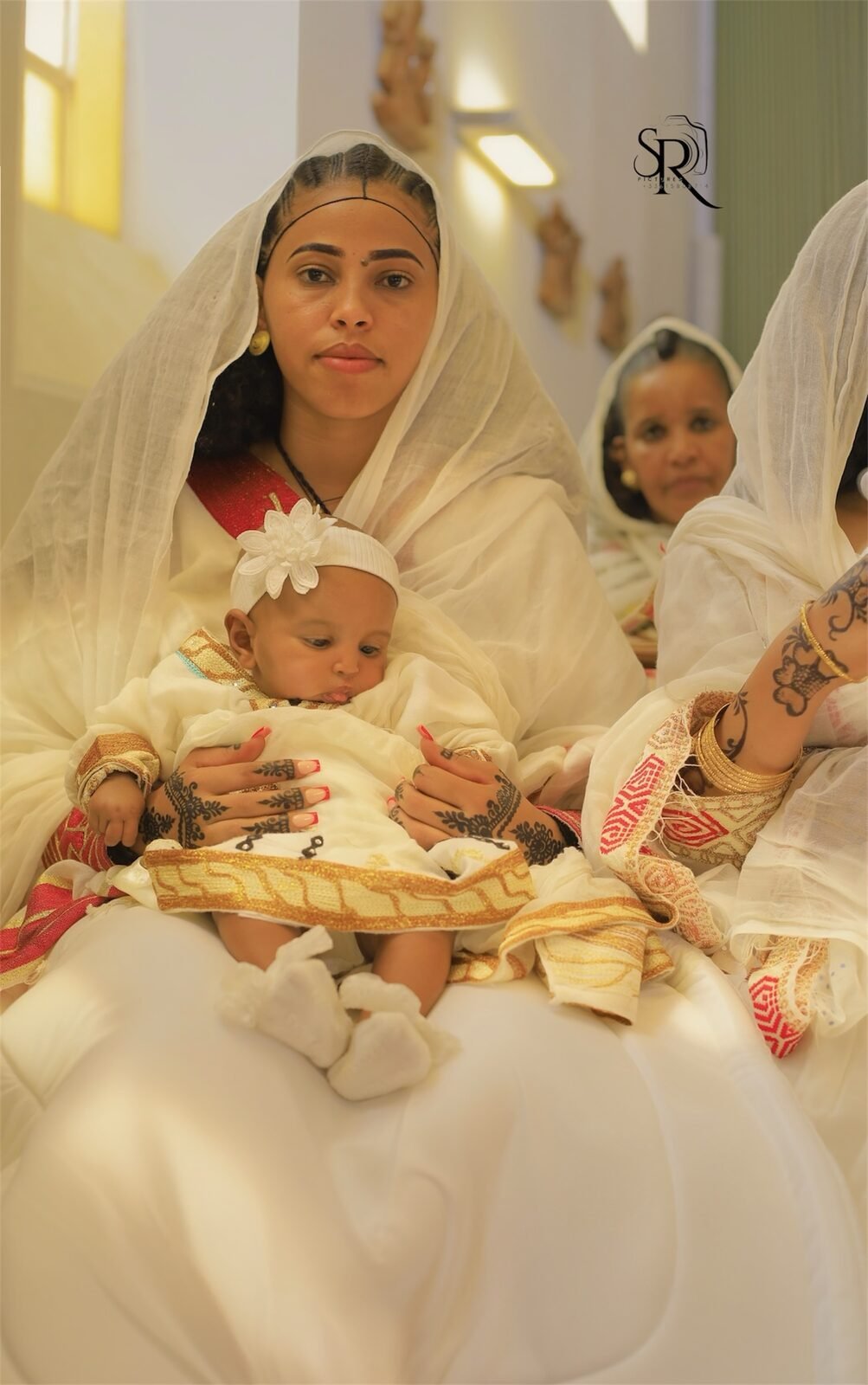 Une femme en tenue traditionnelle tient un nourrisson, une fillette à ses côtés