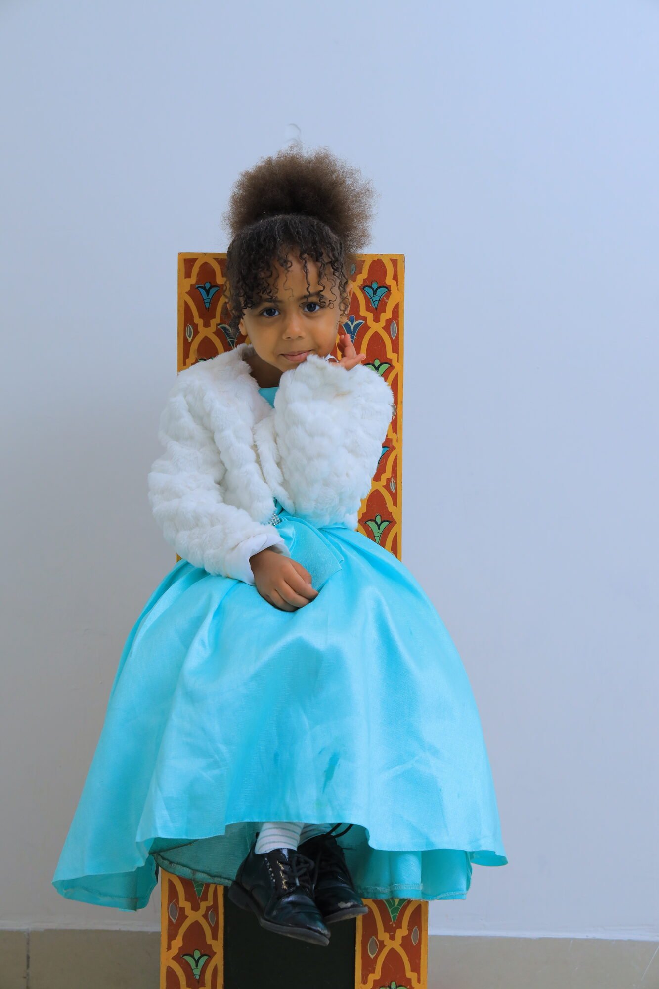 Petite fille en robe bleue assise sur un siège traditionnel